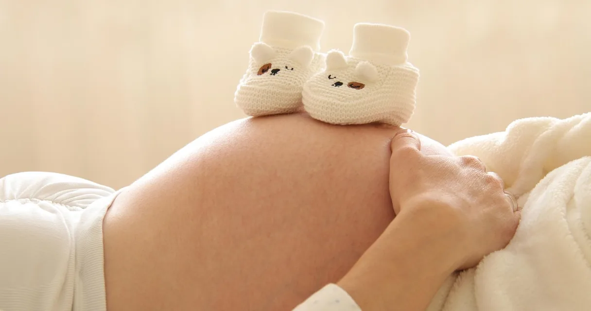 Barriga de gestante com um par de sapatinhos de bebê apoiado sobre ela